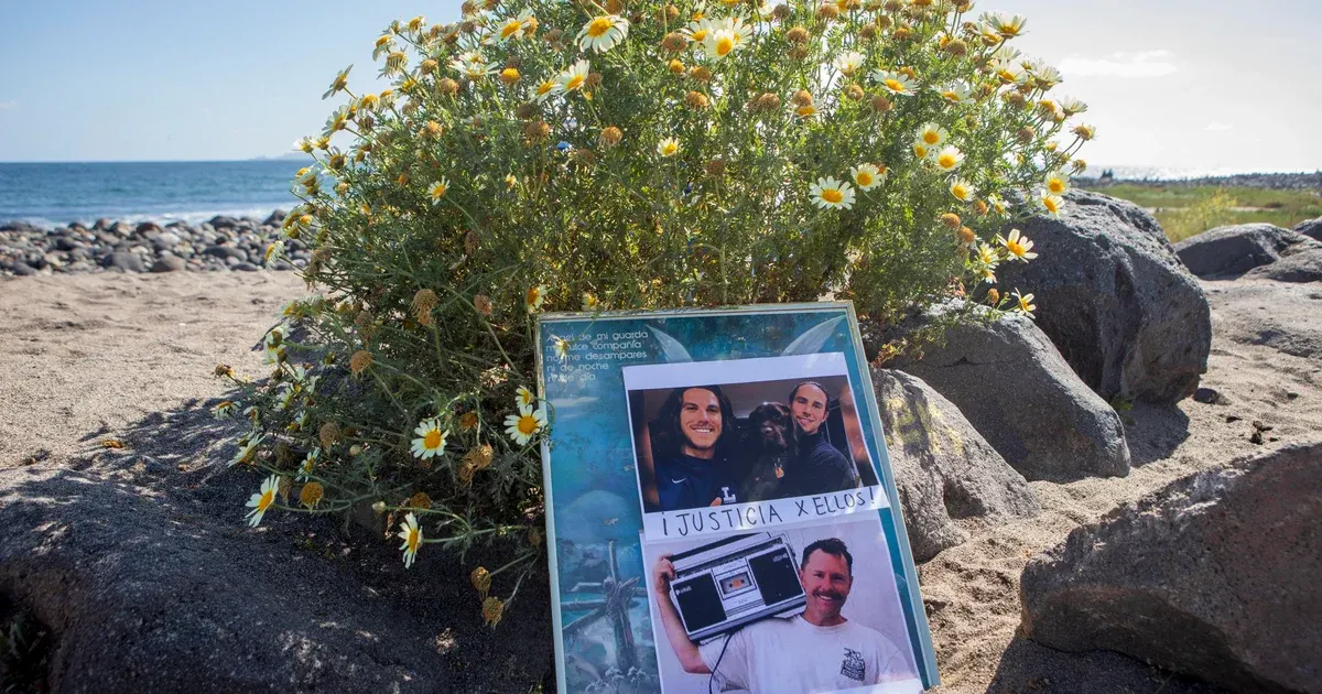 Memorial photo frame with portraits and handwritten message on a beach, flowers and rocks nearby