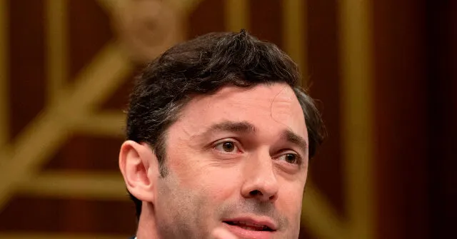 Close-up of a man with dark hair speaking, ornate gold-patterned wood backdrop behind him.