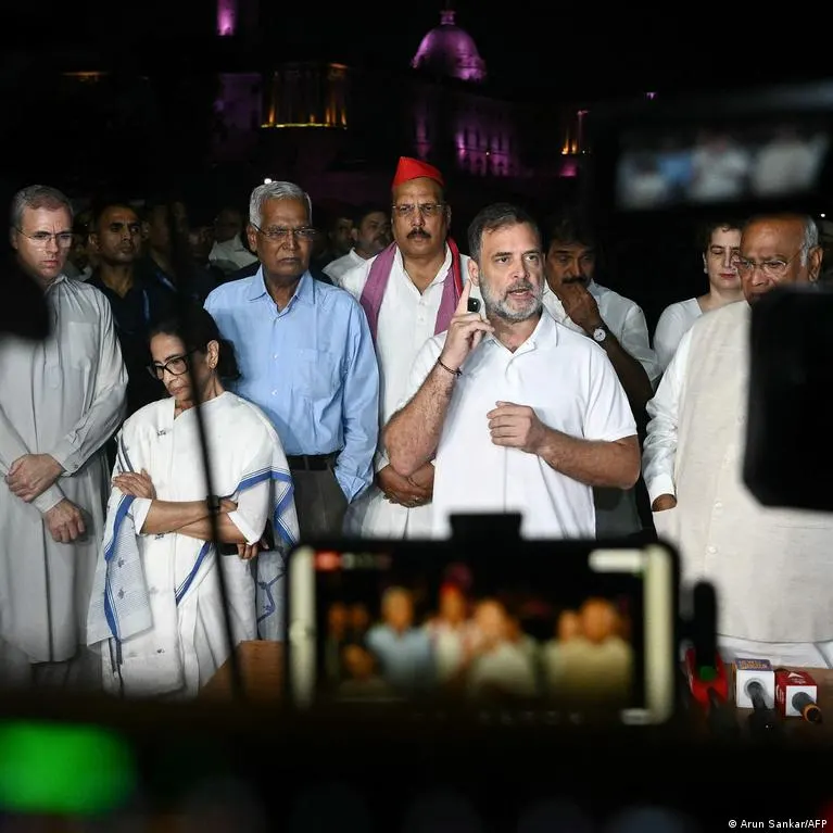 Group of politicians at night in front of an illuminated building, one man speaking and gesturing to a crowd.