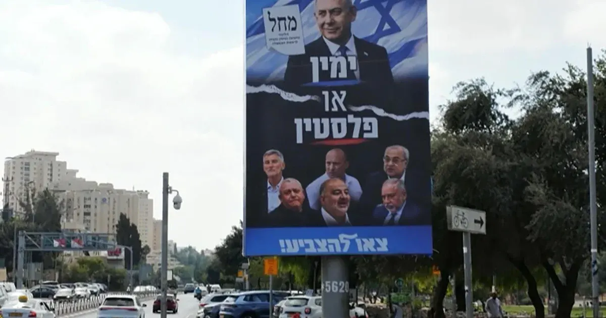 Large Israeli election campaign billboard over a street with a flag, several candidate portraits and traffic below.