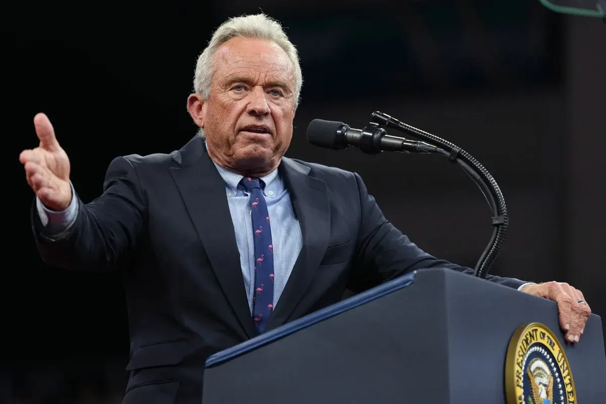 Older man in dark suit gesturing while speaking at a podium with presidential seal.