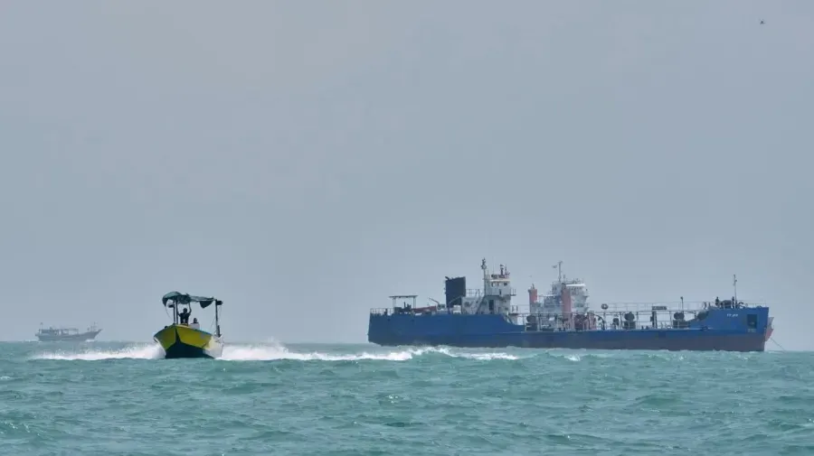 Blue oil tanker and small yellow boat on choppy grey sea under hazy sky