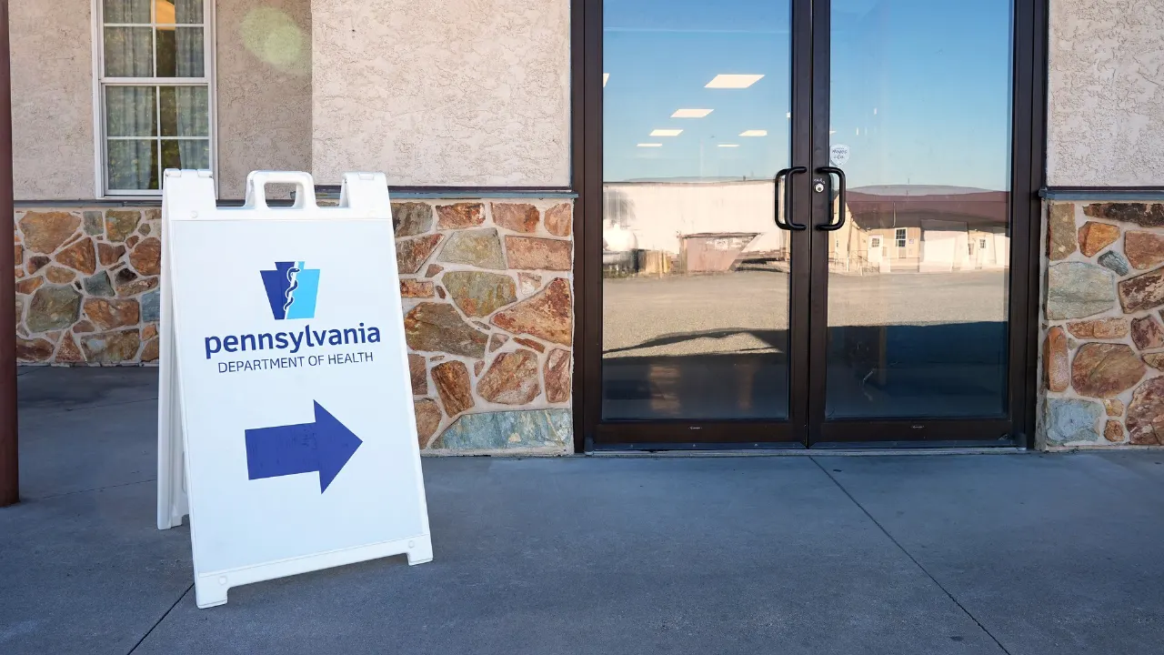 Pennsylvania Department of Health sidewalk sign with arrow outside glass doors of a building.