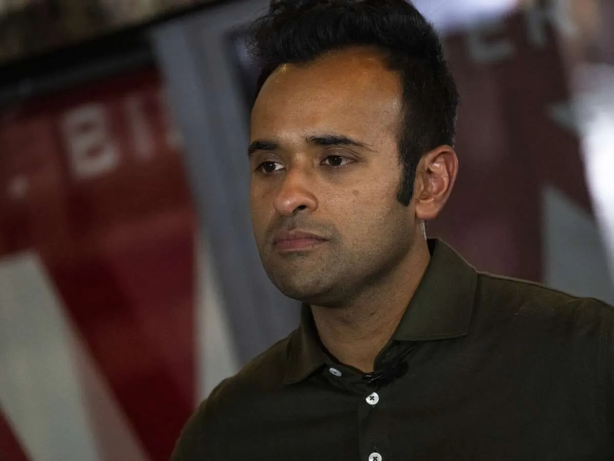 Man in dark olive shirt with blurred red and white banner behind him, looking to the side