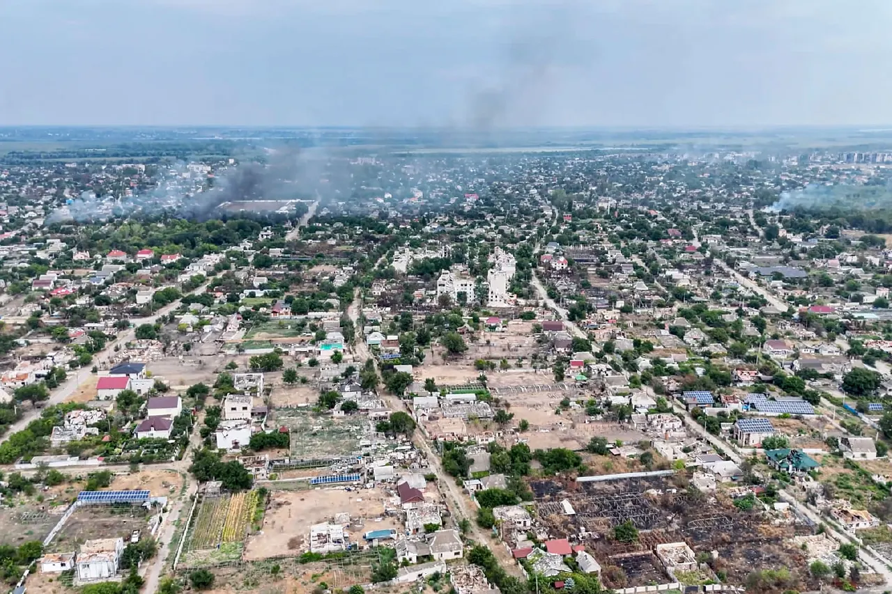 Aerial view of a town with smoke rising from damaged, burning buildings in the distance.