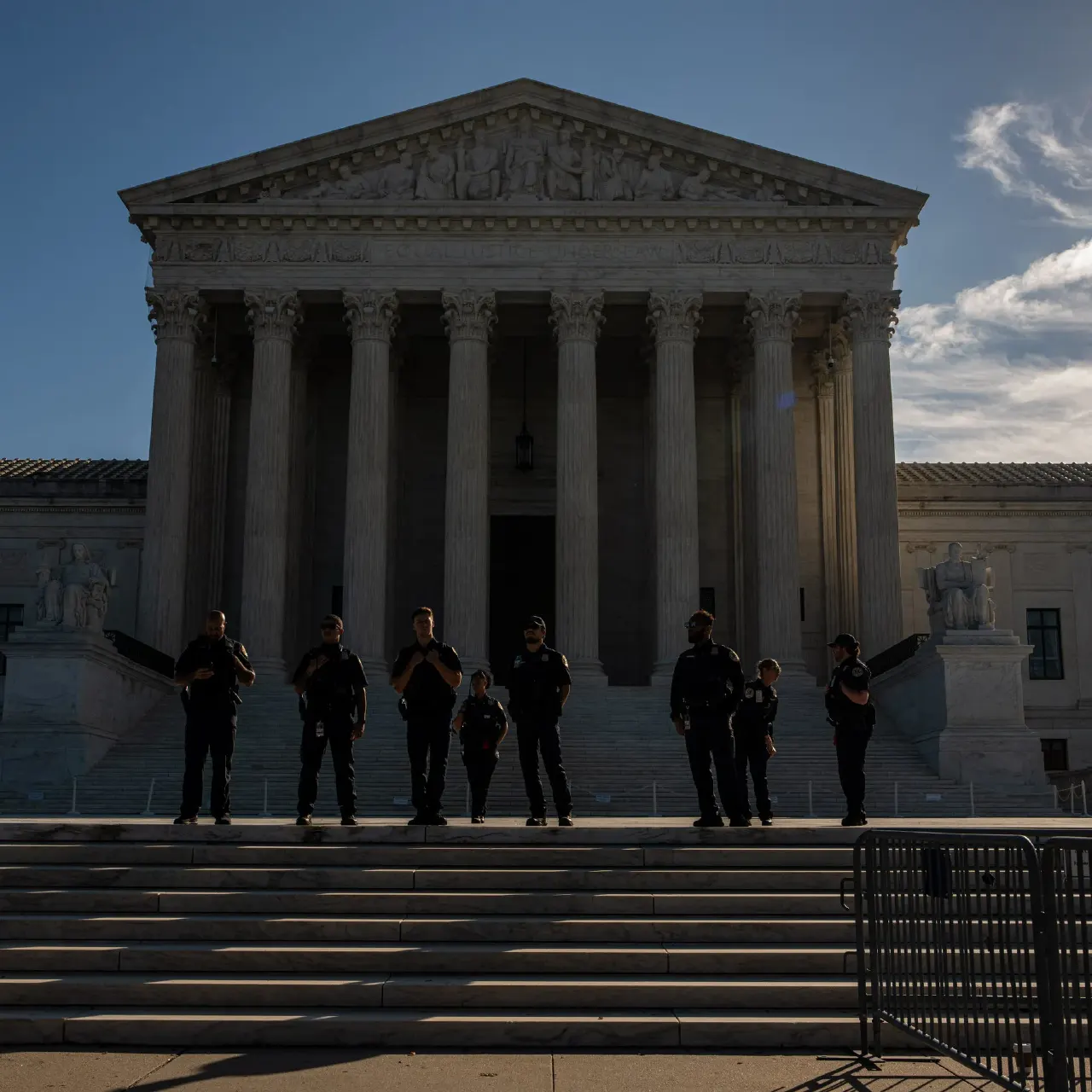 Supreme Court building facade with columns, officers standing on steps at dusk.