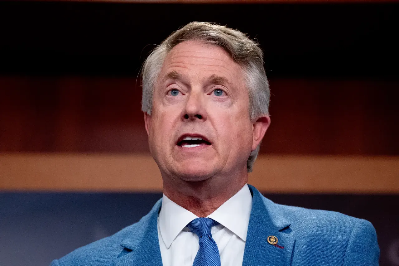 Man with gray hair in blue suit and tie speaking at a press event.