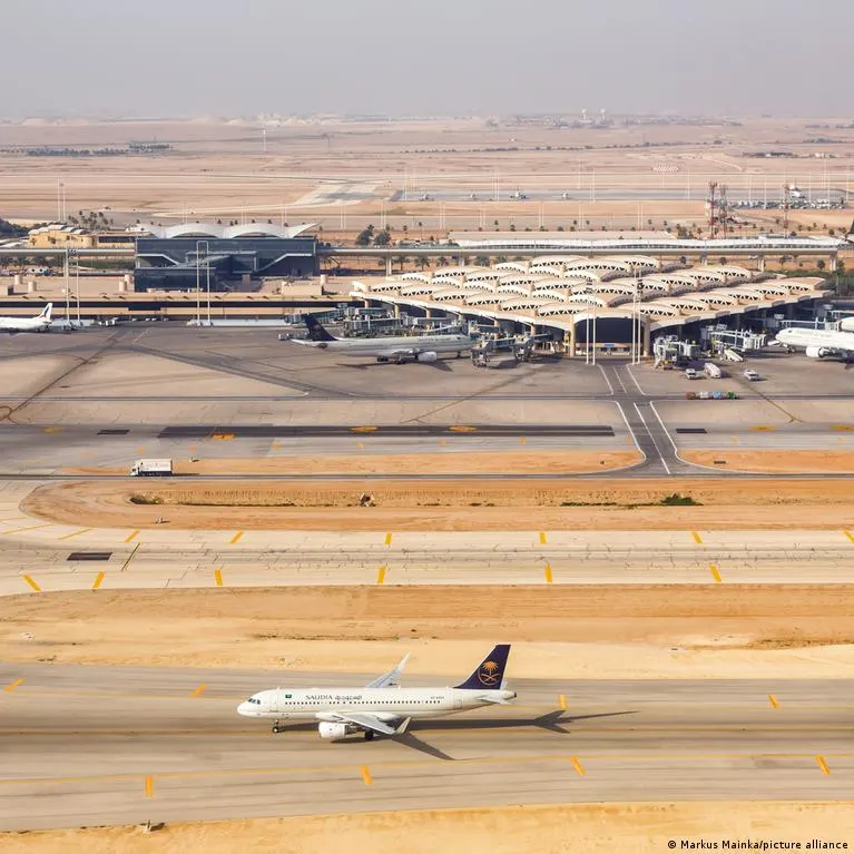 Aerial view of airport terminal and runway with a Saudia jet taxiing in desert setting