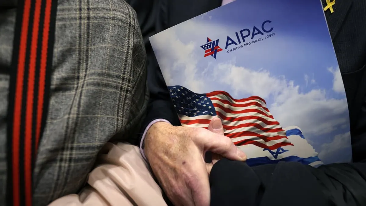 Close-up of a hand holding a brochure with AIPAC logo and US and Israeli flags