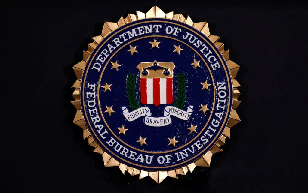 Gold and blue Federal Bureau of Investigation seal reading Department of Justice on dark background.