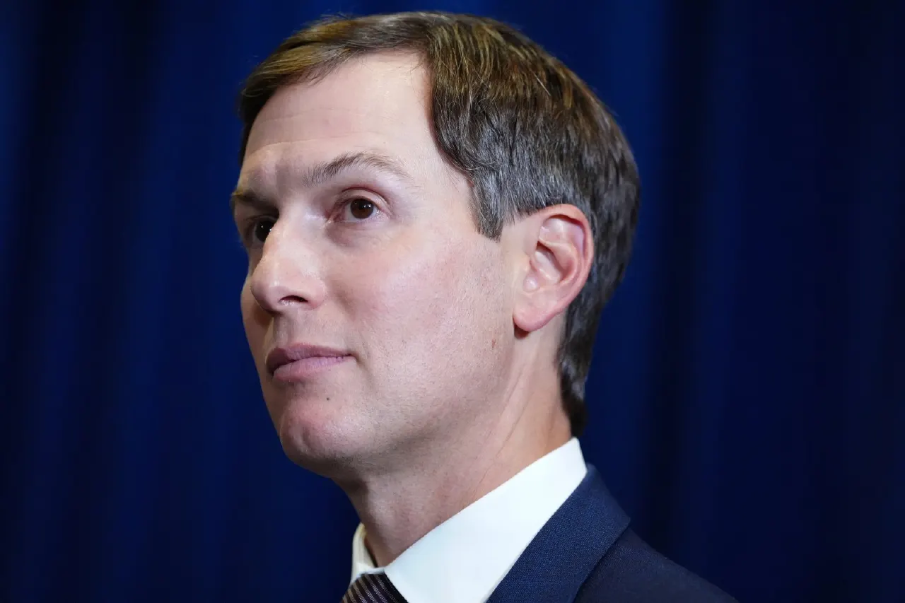 Man in dark suit and white shirt against a blue curtain, looking off to the side.