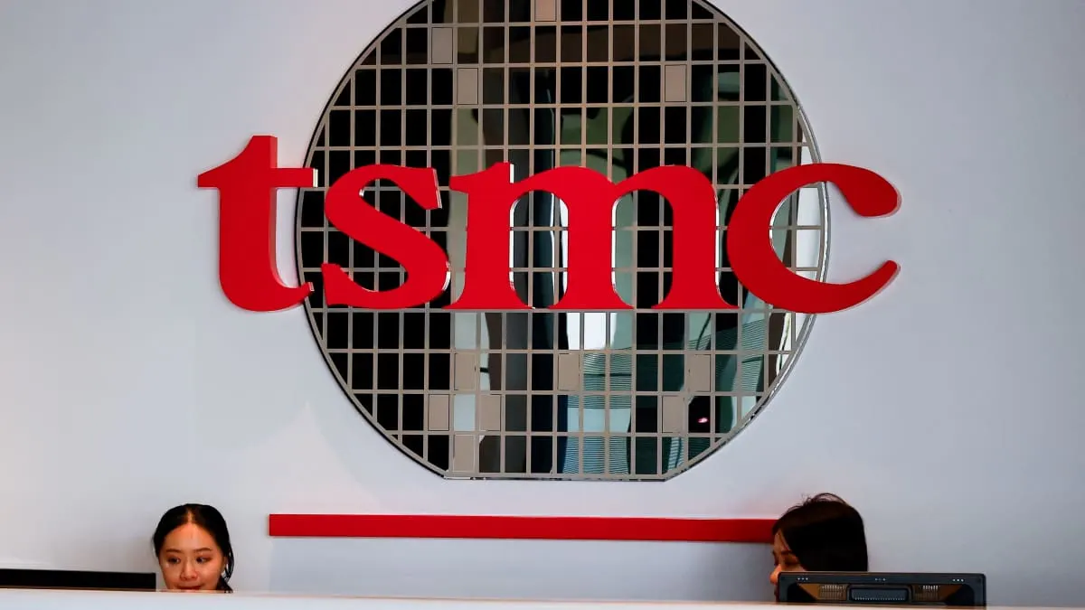 Red TSMC logo on a wall above a reception desk, with two staff partly visible.