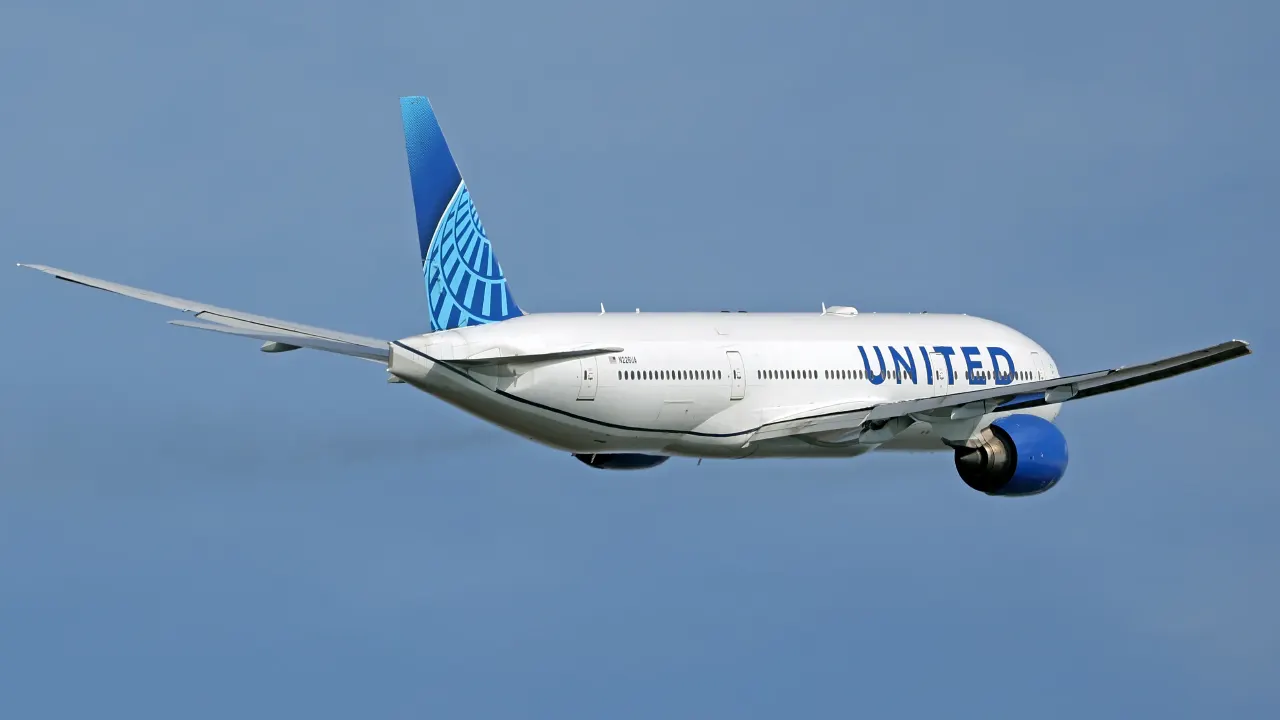 United Airlines jet in flight against a clear blue sky, showing its livery and tail.