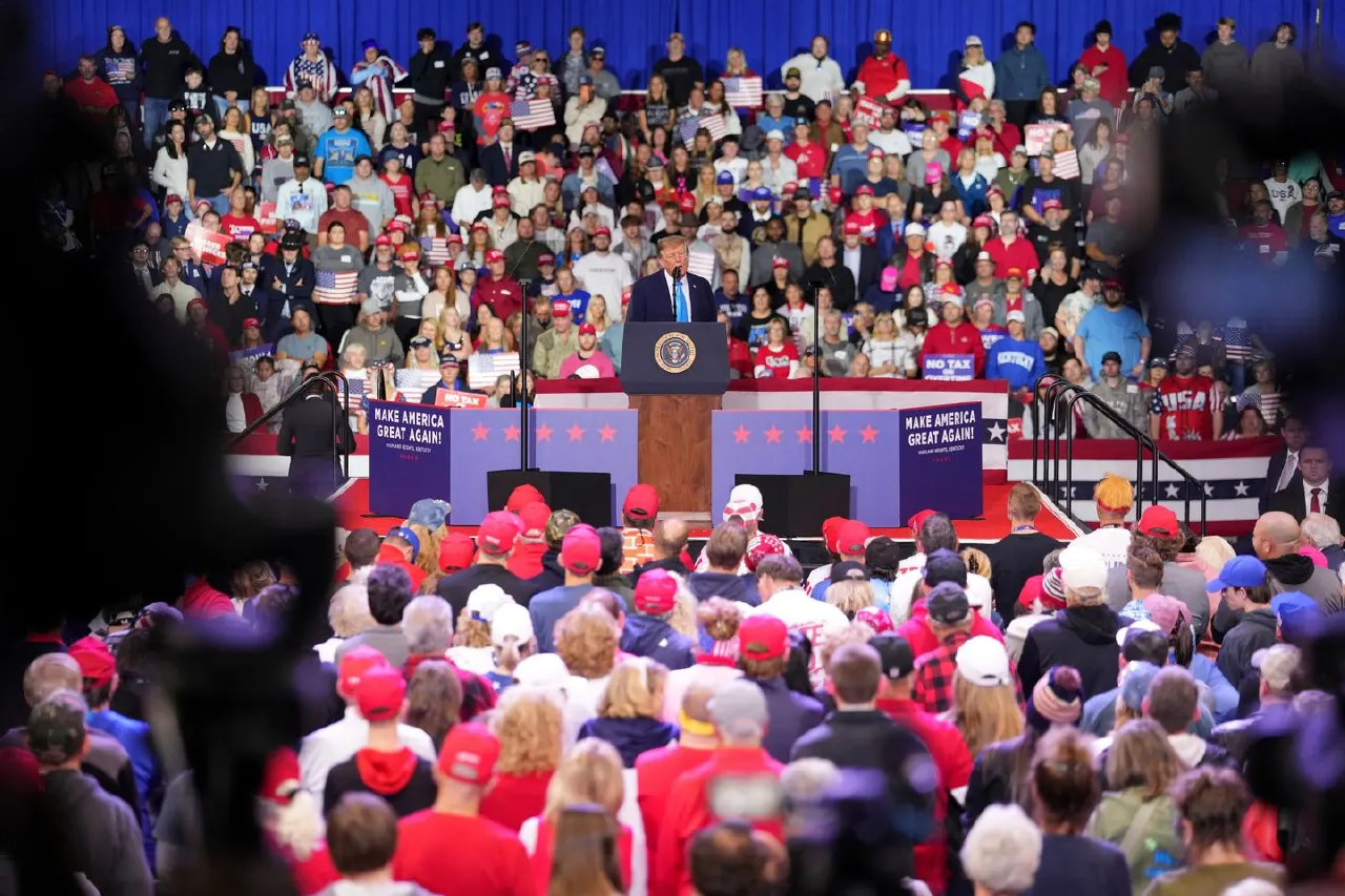Large rally crowd in red caps and flags facing a podium with 'Make America Great Again' signs.