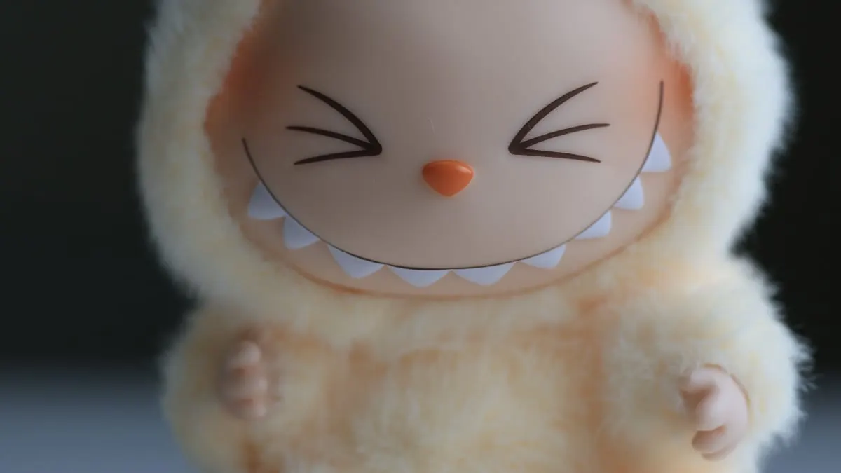 Close-up of a fluffy cream plush toy with a toothy grin and closed eyes.