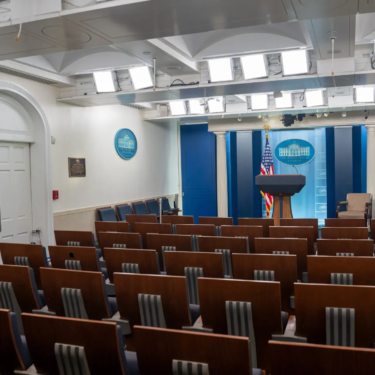 Empty White House briefing room with rows of seats facing a podium and seal.