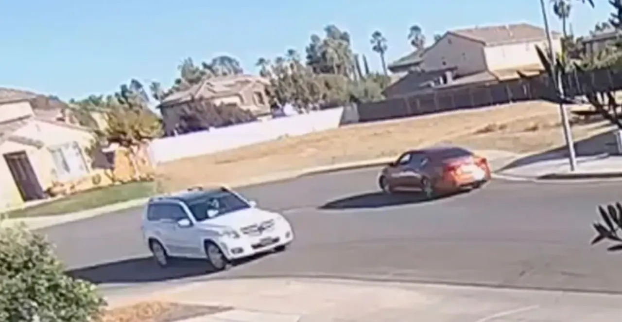 Surveillance-style footage of a white SUV and a dark red sedan turning on a suburban residential street
