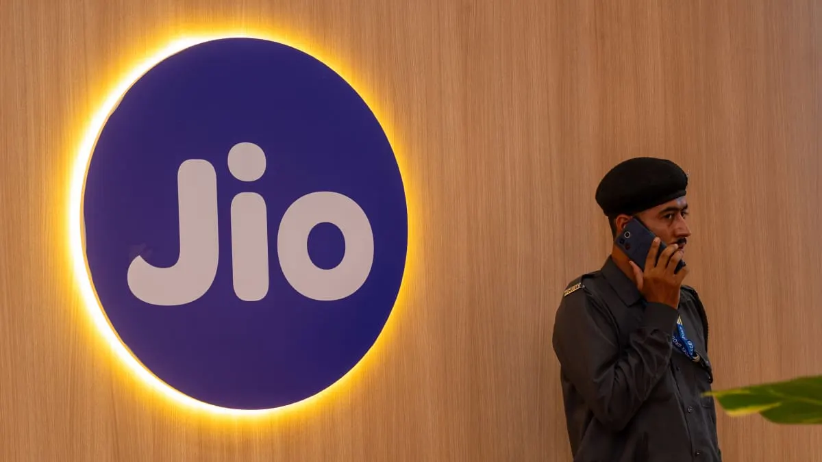 Illuminated Jio logo on wooden wall beside uniformed guard speaking on phone