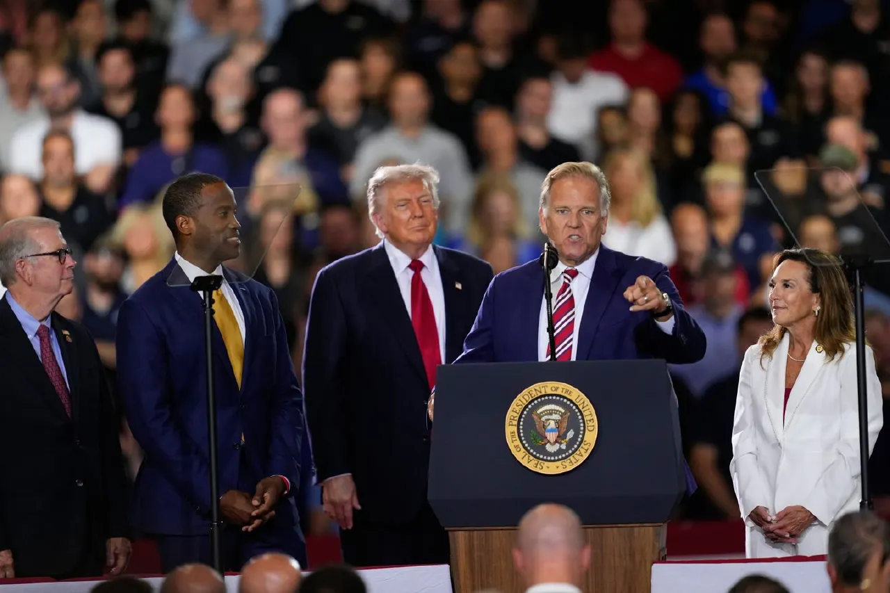 Men on a stage at a podium bearing the presidential seal, before a crowded audience.