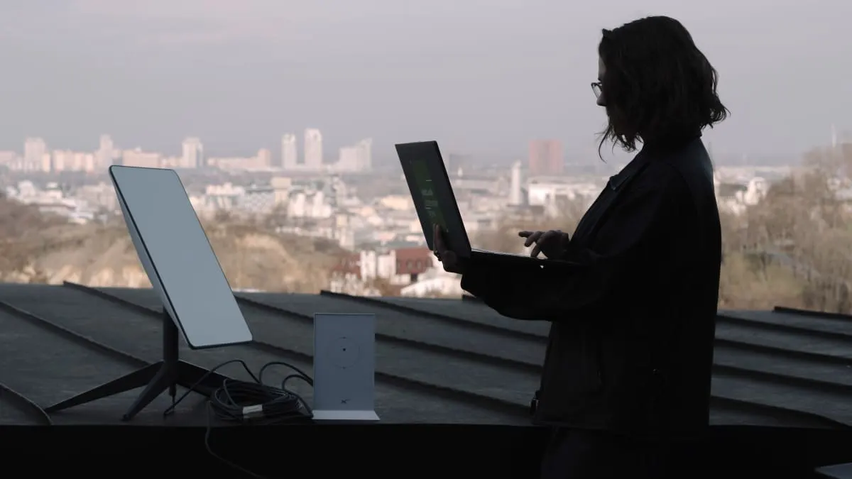 Silhouetted woman with laptop beside a satellite terminal overlooking a city skyline