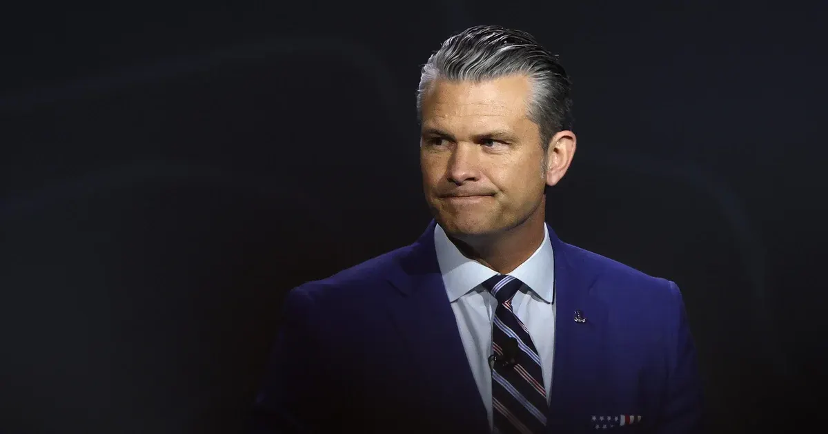 Man in navy suit and striped tie against dark background, looking off to the side.