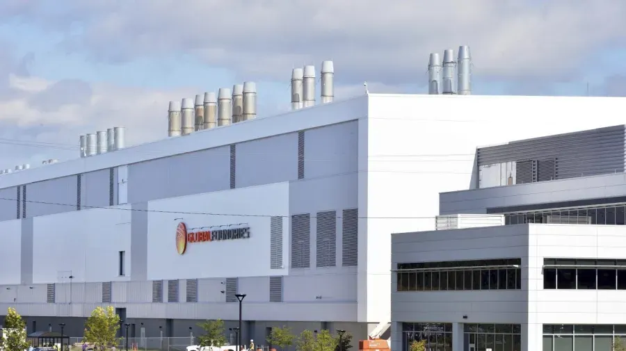 Large white GlobalFoundries semiconductor factory with exhaust stacks and company logo on the facade.
