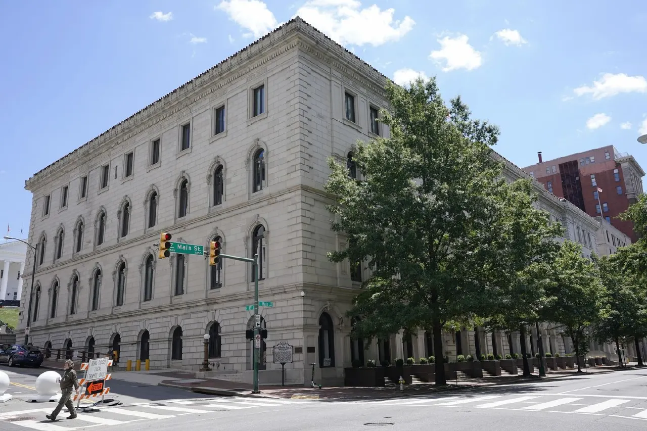 Large stone courthouse-style building on a sunny street corner, with a pedestrian crossing and traffic light.