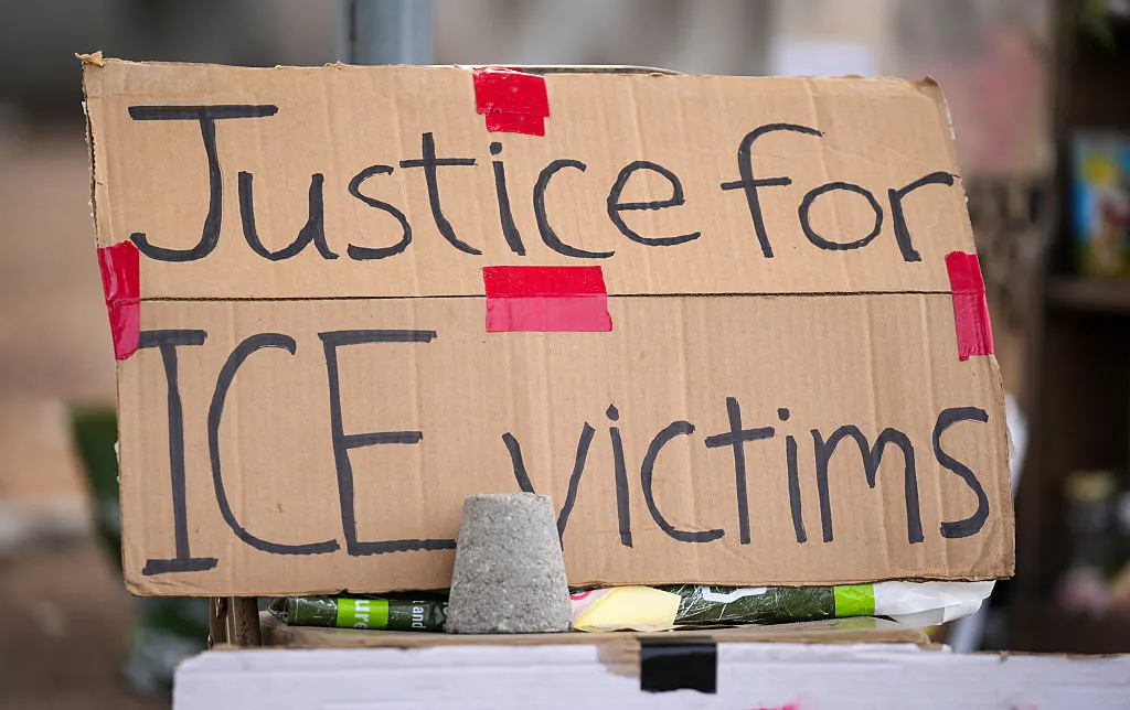 Cardboard protest sign reading "Justice for ICE victims" taped to a makeshift stand with a stone.