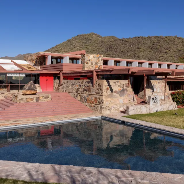 Stone and red-trimmed desert building with pool, Frank Lloyd Wright style, mountains behind