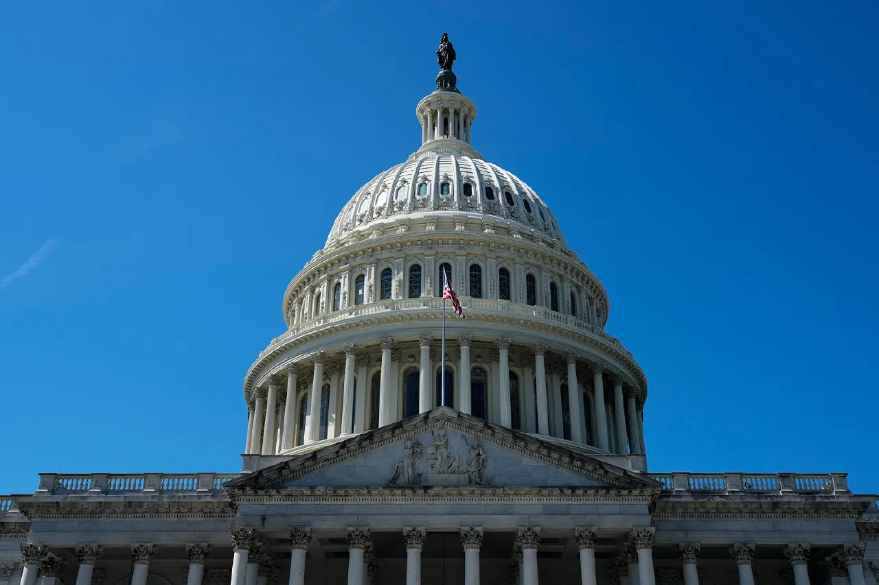 The U.S. Capitol dome and facade under a clear blue sky, with an American flag.