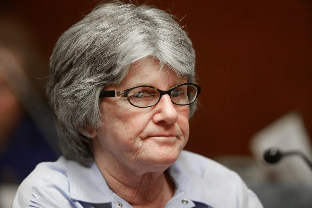 Older woman with gray hair and glasses in a hearing room, microphone nearby.