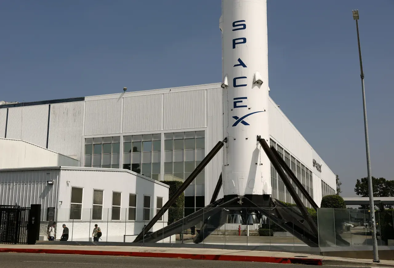 SpaceX rocket on display in front of white company facility building with glass windows