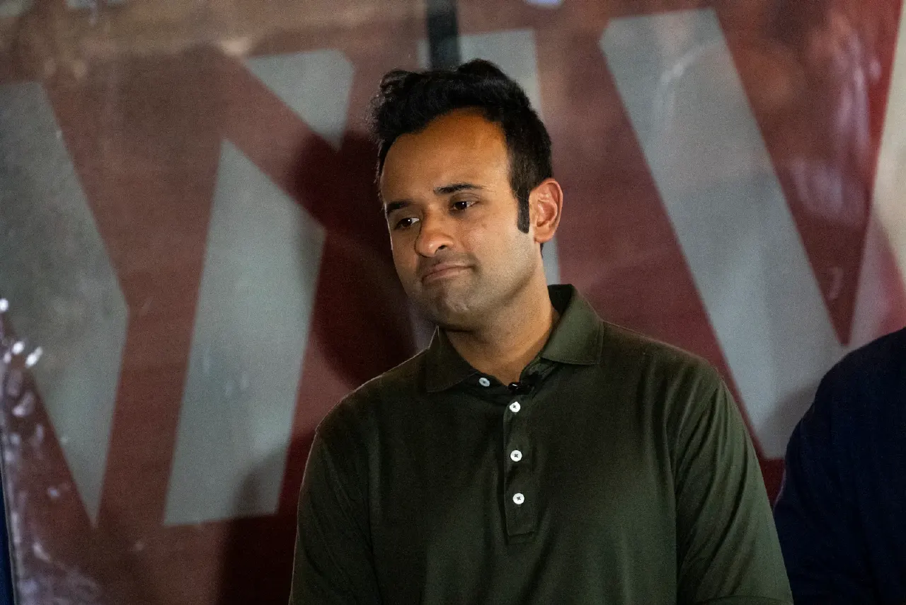 Man in dark green polo shirt with pursed lips in front of red and white backdrop.