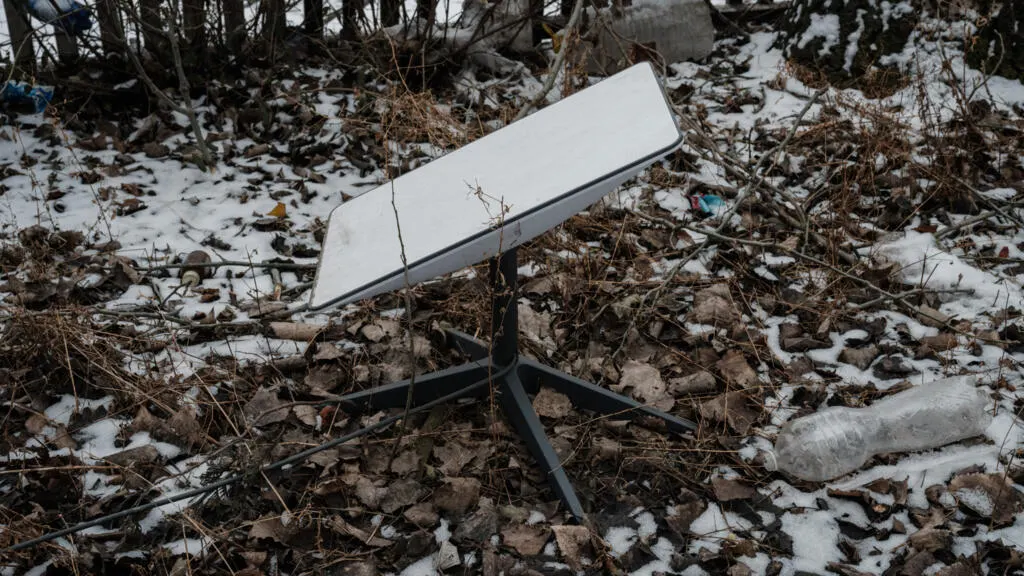 White flat satellite terminal dish on tripod in snowy, leaf-strewn wooded ground