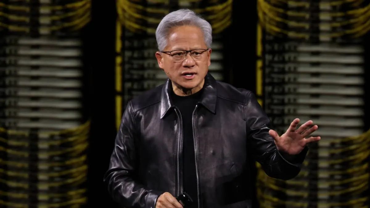 Silver-haired man in leather jacket and glasses gesturing while speaking on a stage