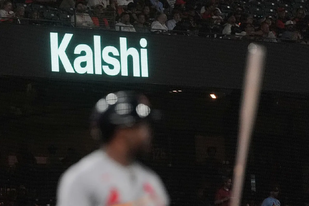 Blurred baseball player in helmet at bat beneath illuminated Kalshi sign in stadium.