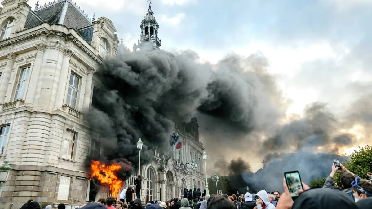 Black smoke and fire at a French town hall during crowd unrest, people filming.