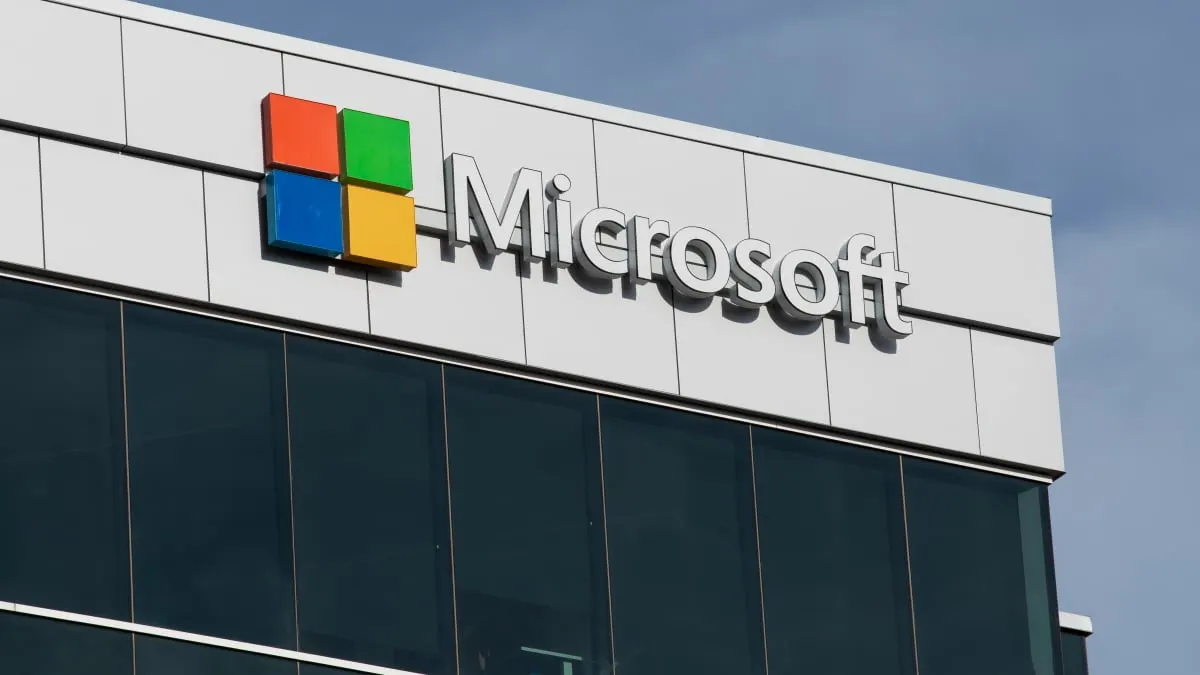 Microsoft logo and name on the facade of a glass office building against blue sky