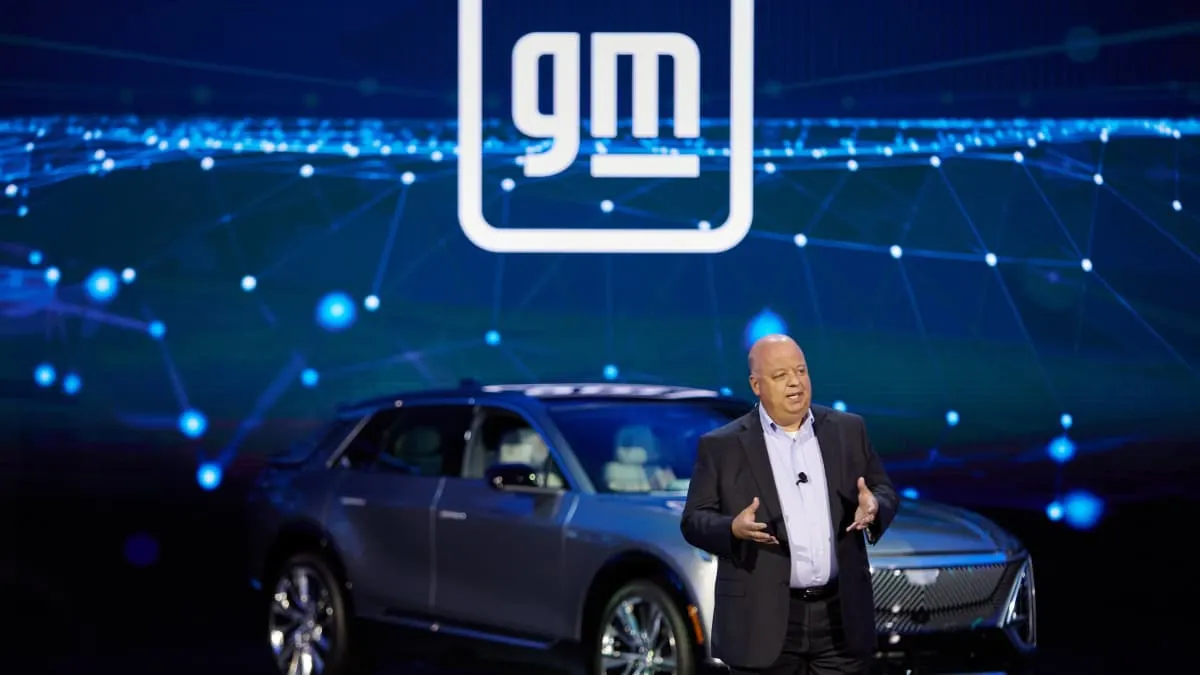 Man speaking on stage before large GM logo and a silver electric SUV.