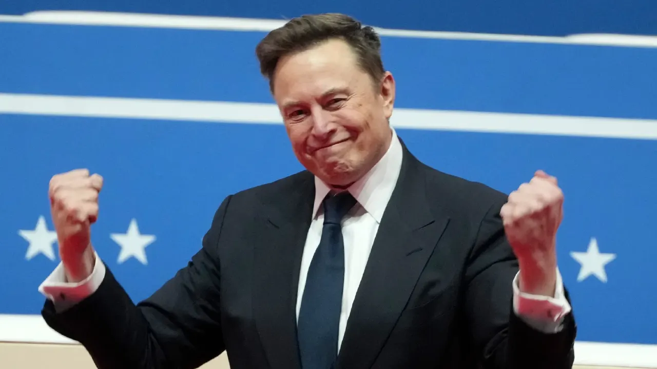 Man in dark suit clenching fists and smiling in front of blue star backdrop.