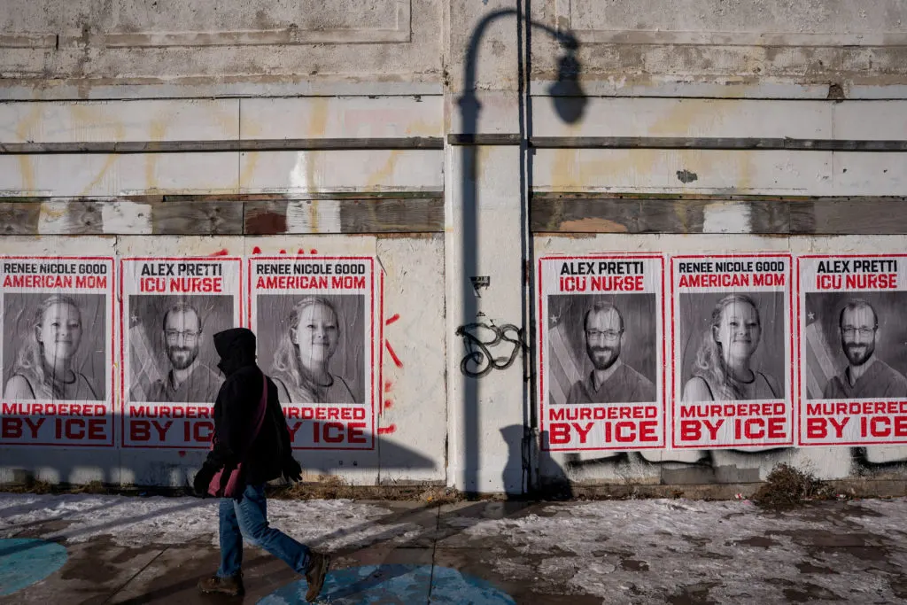 Pedestrian walks past wall of protest posters with red-bordered portraits reading murdered by ICE.