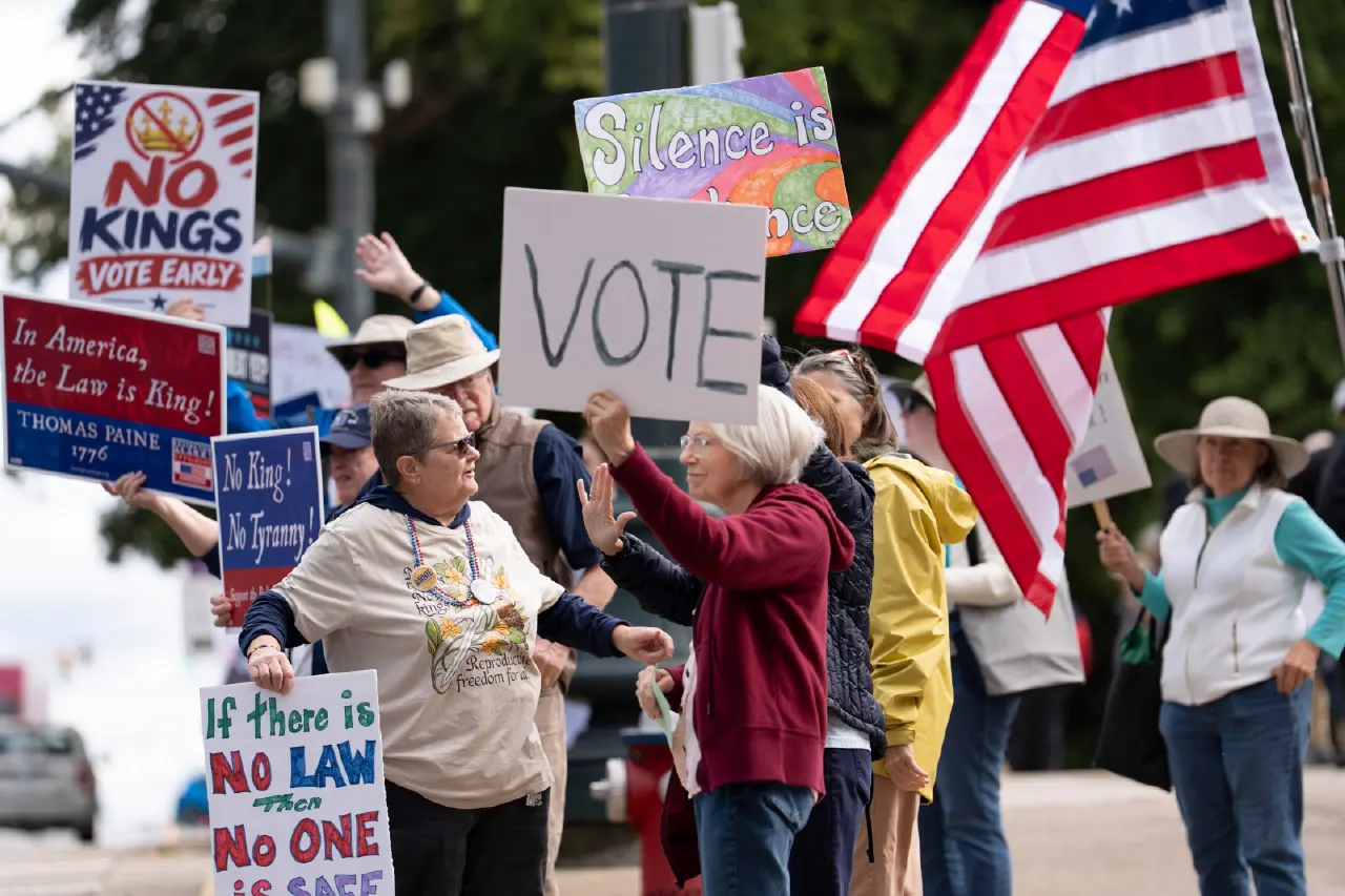 Protesters on a street holding No Kings and Vote signs, with American flags.