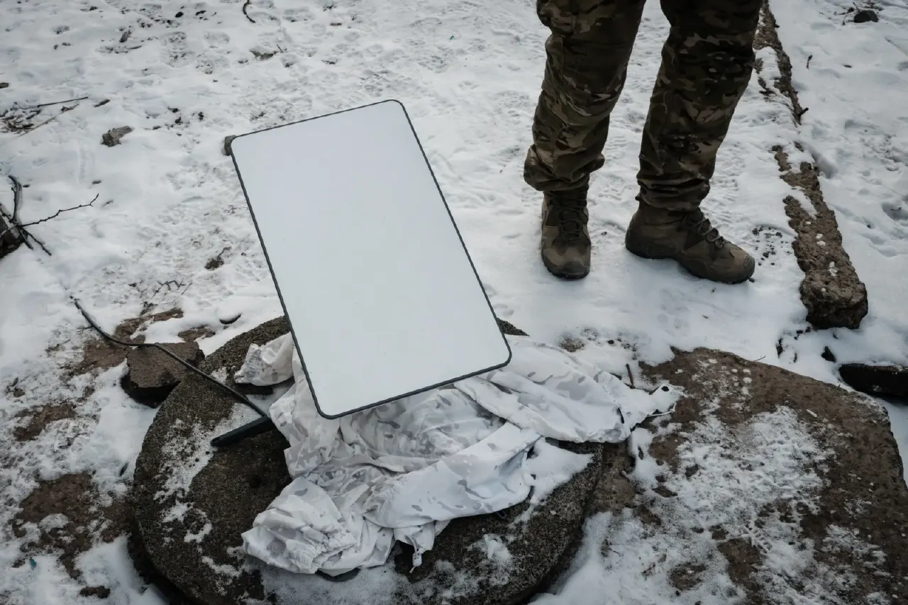 Blank white satellite dish terminal on snowy ground, with a soldier's camouflage boots beside it.