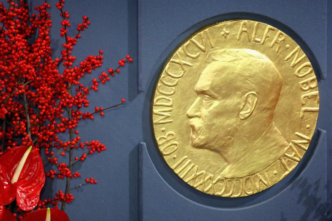 Gold Nobel Peace Prize medallion with Alfred Nobel profile beside red berries and anthuriums.