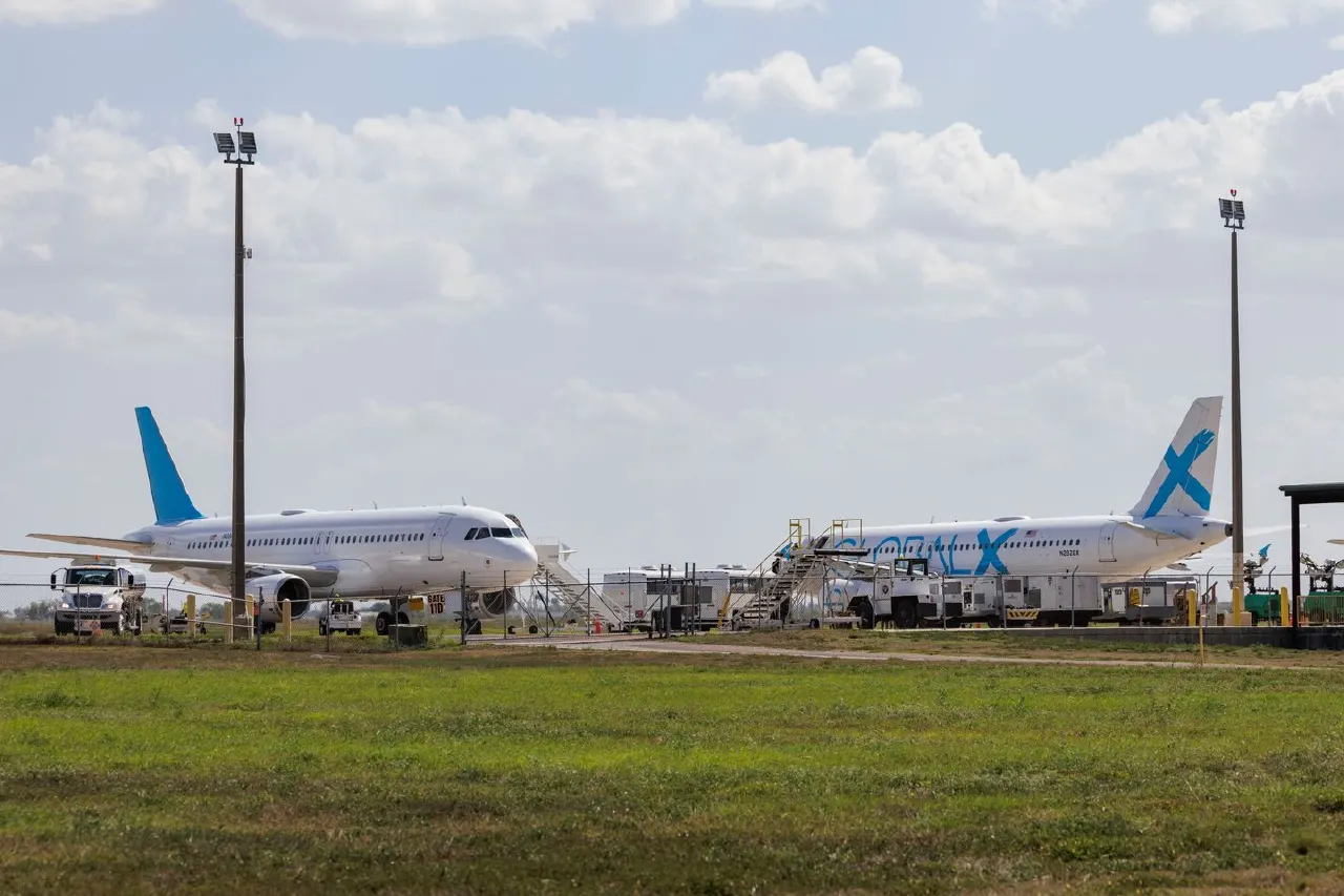 Two white passenger jets parked on an airport apron with ground service vehicles and stairs.