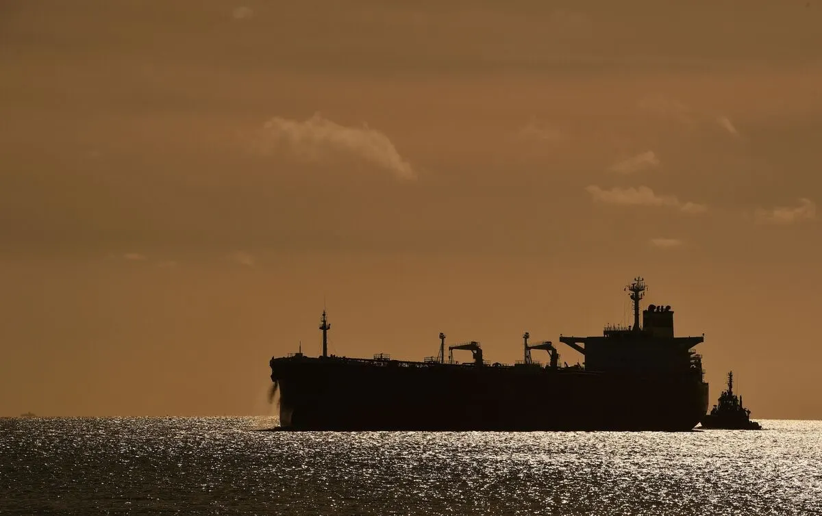 Silhouetted oil tanker at sea at sunset, with a tugboat alongside.