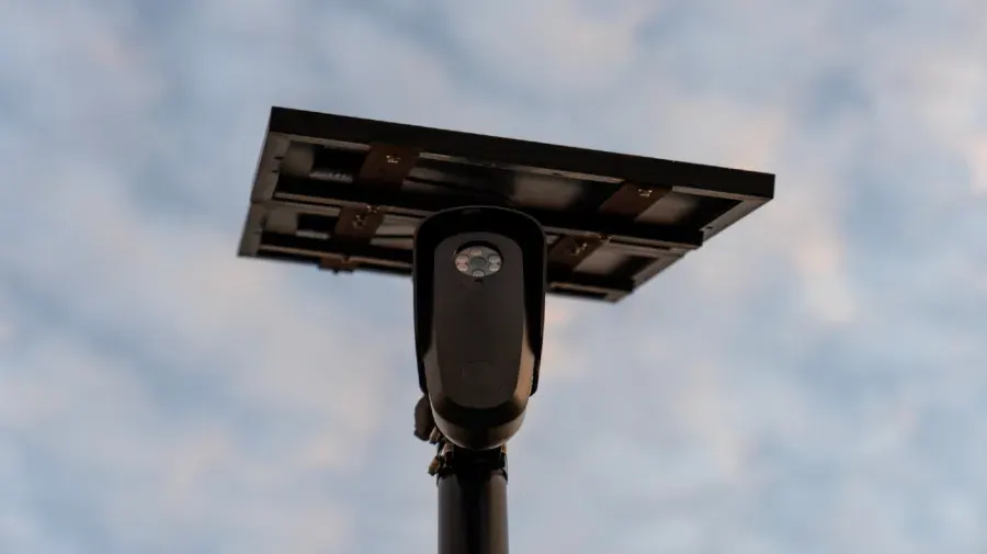 Low-angle view of a solar-powered security camera on a pole against cloudy sky.