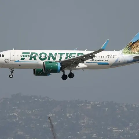 Frontier Airlines jet in green livery with jaguar tail landing over hillside city.