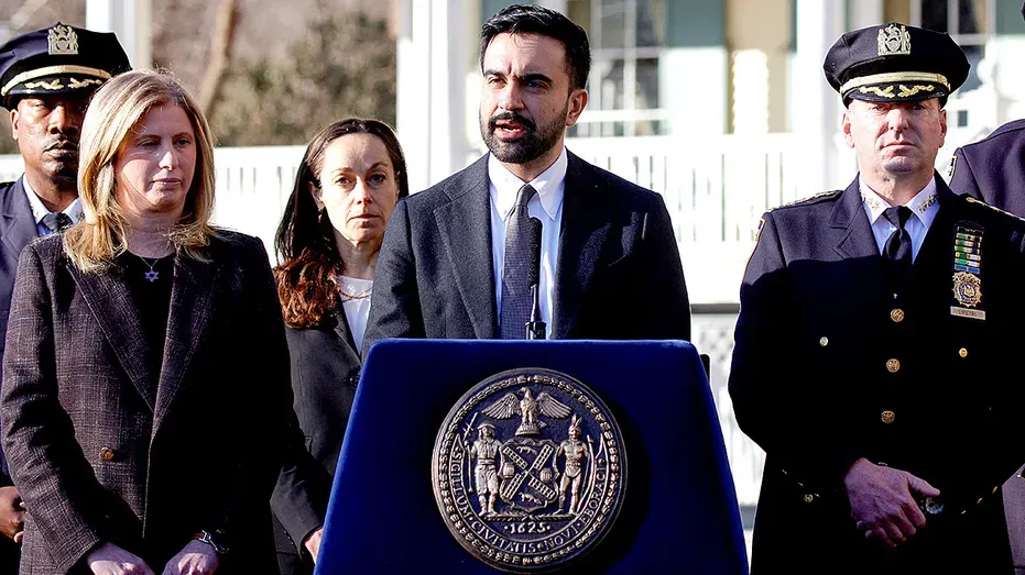 Man speaking at podium with city seal beside uniformed police officers and officials outdoors.