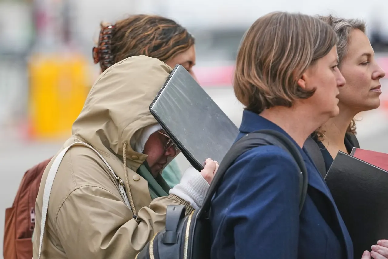 Women walking outside carrying folders, one with hood up hiding face